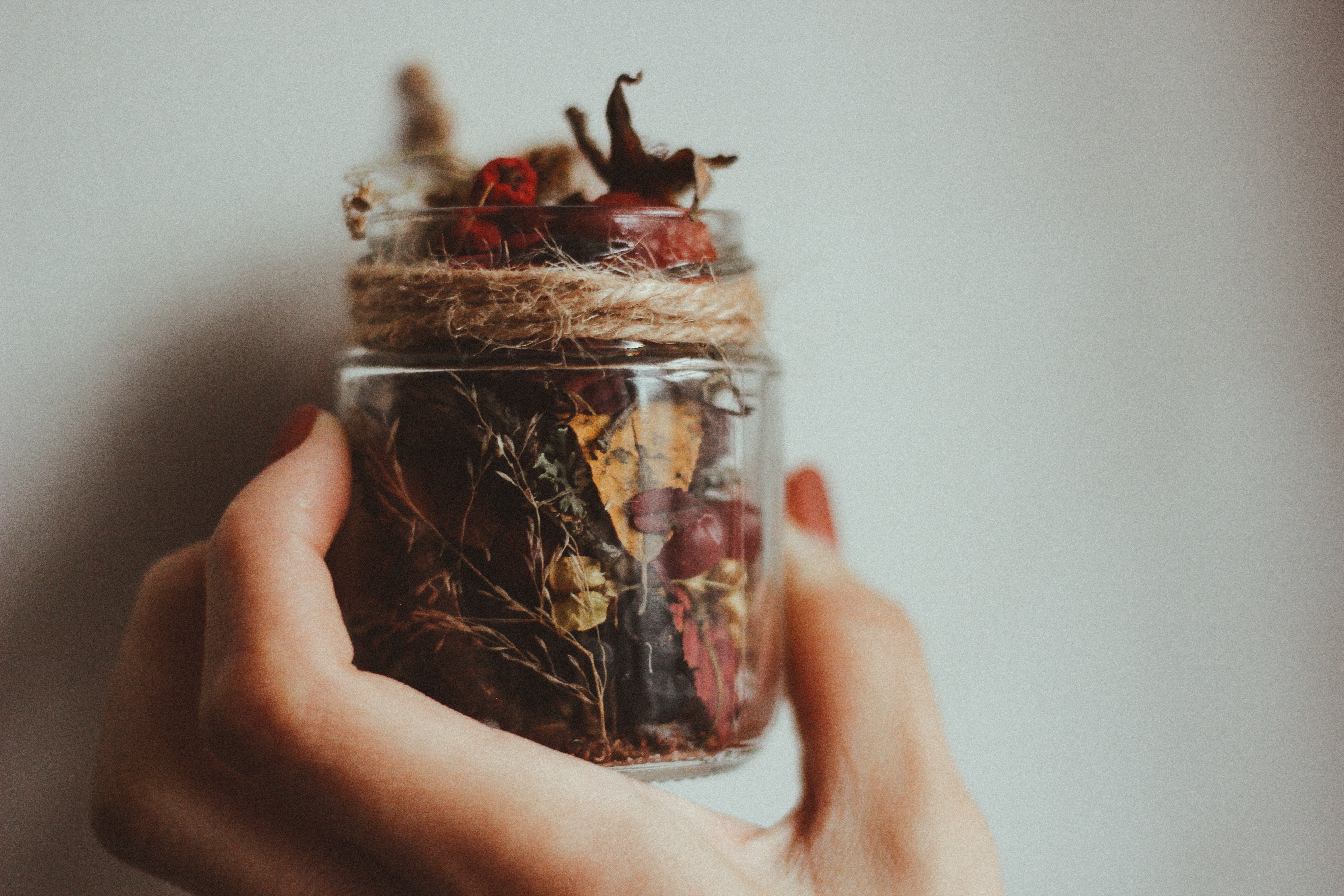 a hand holding a small jar full of dried berries and leaves